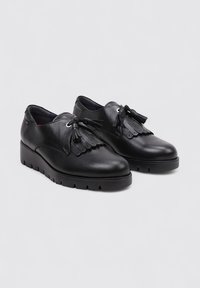 Zapatos de cuero negros con un tacón bajo, que presentan una punta redondeada, borlas decorativas y un diseño de cordones. Superficie texturizada con un sutil brillo.