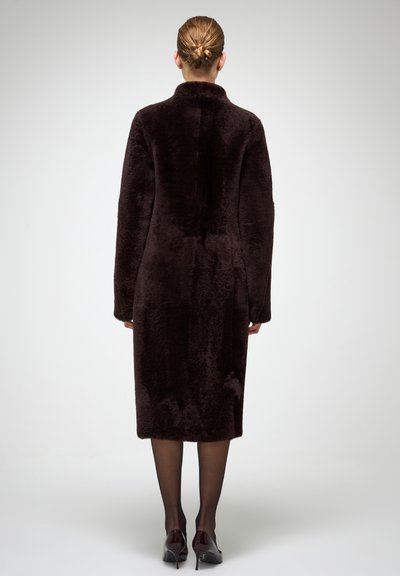 Garš, tumši brūns mākslīgās kažokādas mētelis ar augstu apkakli un pilnām piedurknēm, sniedzas līdz viduskulbam, ar teksturētu virsmu, bez redzamiem aizdares elementiem.