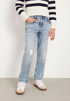 Jeans in denim azzurro chiaro, dritti e con dettagli strappati. Abbinati a sneaker bianche con accenti beige e un maglione corto a righe blu navy.