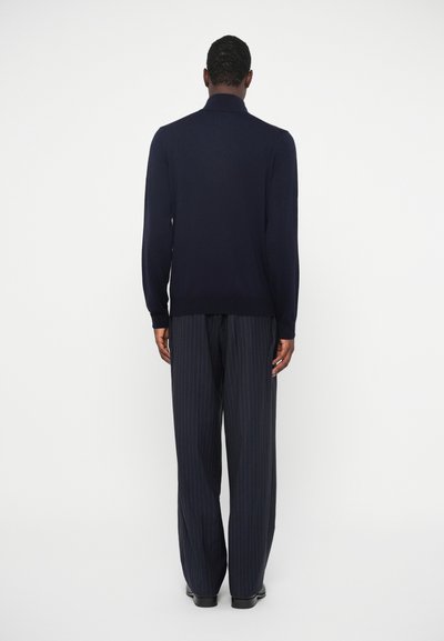 Granatowy sweter dzianinowy z kołnierzykiem, zestawiony z szerokimi spodniami w paski. Ubranie charakteryzuje się jednolitą kolorystyką i gładką fakturą.