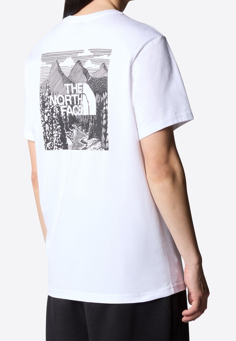 Person wearing a white t-shirt with a black and white mountain and forest graphic and "The North Face" logo on the back.