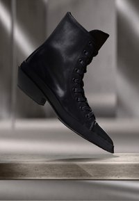 Schwarzlederne Knöchelstiefel mit Schnürdesign, spitzem Zehenbereich und niedrigem Blockabsatz. Glatte Textur mit matter Oberfläche.