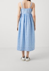 Ljusblå bomullsmaxi klänning med justerbara axelband, samlad midja och stjärnbroderi. Bärs med vita sneakers med svarta detaljer.