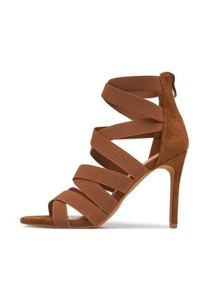 Rudos zomšos aukštakulniai sandalai su keliais plačiais audinio dirželiais, atviru pirštu ir siauru kulnu, suteikiančiu papildomą aukštį.