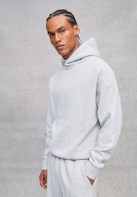 Felpa grigia realizzata in tessuto morbido, con scollatura ampia e maniche lunghe. Abbinata a pantaloni della tuta grigi coordinati. Design semplice e casual.