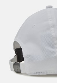 Hvid kasket lavet af tekstureret stof, med en buet skygge, justerbar strop bagtil og en metalaccent med et logo.