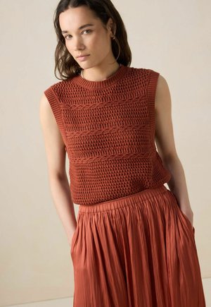 Roestkleurig, mouwloos gebreid topje met textuurrijke patronen, gecombineerd met een plooienrok met elastische taille in bijpassende kleur.