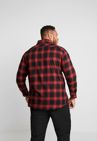 Rood en zwart geruite flanellen shirt met lange mouwen en een puntige kraag. De stof heeft een zachte textuur met een iets vrijere pasvorm.