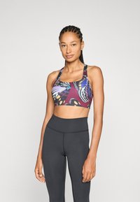 Sujeción deportiva de color púrpura con un patrón de mariposas, hecha de tela elástica. Combinada con leggings negros de tiro alto, de textura suave y diseño ajustado.