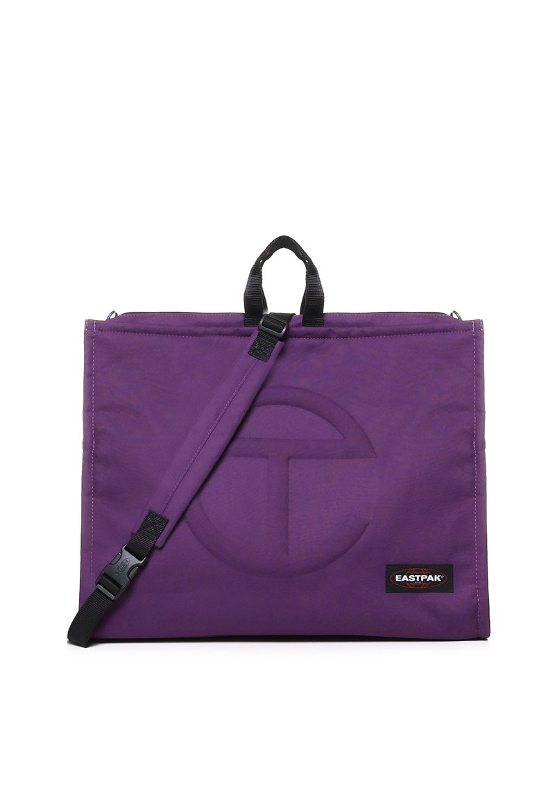 Sac en bandoulière violet avec une texture douce, un design plat, des poignées supérieures et une bandoulière ajustable. Comprend un logo en relief et une étiquette de marque.