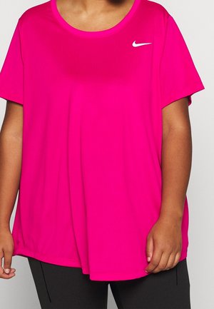 Personne portant un t-shirt de sport manches courtes Nike rose vif et un pantalon noir, debout devant un fond clair uni.