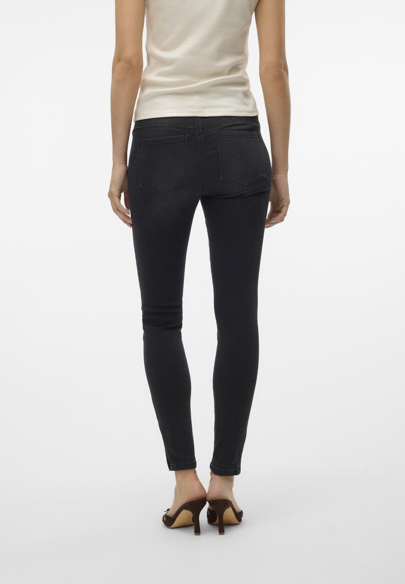 Donkere skinny jeans met een gladde textuur, achterzakken en een hoge taille, gecombineerd met bruine hakken en een aansluitend crèmekleurig topje.