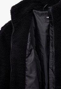 Czarna polarowa kurtka, miękka w dotyku, z zapięciem na zamek z przodu, wewnętrzna podszewka w czarnym materiale, widoczna metka z informacjami o rozmiarze, brak zewnętrznych szczegółów.