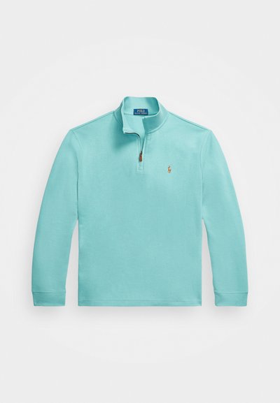 Pullover azul claro com um fecho de zíper de um quarto, mangas longas e um pequeno logótipo bordado no lado esquerdo do peito. Textura suave.