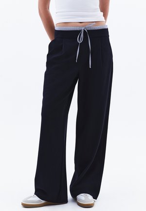 Navy wide-leg pants made of soft fabric, featuring a drawstring waist with a striped accent, and front pockets. Paired with white sneakers.