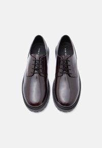 Λαμπερά μπορντό δερμάτινα παπούτσια με στρογγυλή μύτη, δέσιμο με κορδόνια και αντίθετη μαύρη καουτσούκ σόλα; λεία υφή και κομψός σχεδιασμός.