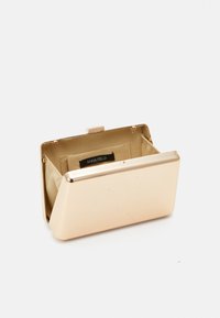 Złota metalowa kopertówka o gładkiej, refleksyjnej powierzchni, w kształcie prostokąta, z beżowym materiałowym wnętrzem z metką.