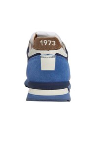 Sininen ja kerma sneaker, jossa on nahan- ja verkkomateriaaleja. Varustettu ruskealla nahan kantapäällä, jossa on "1973" valkoisella. Kumulusmateriaali, pehmustettu kaulus.