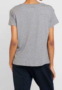 Camiseta de algodón gris con mangas cortas y escote redondo. La parte trasera es lisa, con un ajuste relajado, y presenta una textura suave.