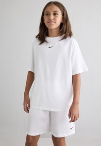 Hvit T-skjorte med korte ermer og svart Nike-logo på brystet, kombinert med matchende hvite shorts med en liten svart Nike-logo.
