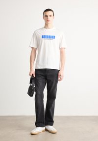 Camiseta de algodón blanca con texto azul "HUGO CREATIVE DEPT.", combinada con jeans de mezclilla negros y zapatillas blancas con acentos beige.