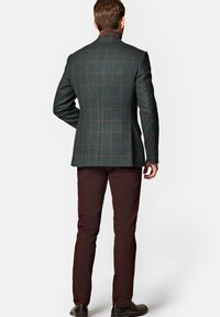 Kurtka w kratę z wełny w ciemnozielonym kolorze z brązowymi akcentami, zestawiona z burgundowymi spodniami. Posiada usztywnione ramiona i dopasowany krój.
