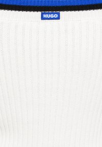 Csíkos kék és fekete nyakkal ellátott bordázott fehér pulóver. A háttal ellátott kék címke "HUGO" hímzéssel. Pamut keverék anyag.
