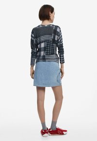 Mustra mustrite jahe- ja halli ruuduline kampsun, millel on erinevad mustrid, koos helesinise teksaseelikuga ja punaste tossudega.