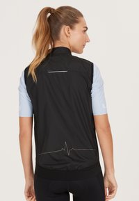 Schwarze ärmellose Weste mit hohem Kragen, aus leichtem Stoff; auf der Rückseite befindet sich ein dezentes Herzschlaglinien-Design.
