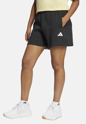 Pantaloni sportivi neri con vita elasticizzata, tasche laterali e logo Adidas bianco. Indossati con scarpe da ginnastica bianche e una maglietta gialla.