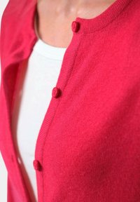 Heldroze cardigan met een gestructureerd breisel, met vijf ronde knopen en een ronde halslijn, gelaagd over een wit shirt.