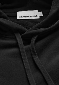 Zwarte hoodie met capuchon en trekkoorden, voorzien van een wit label met de tekst "ARMEDANGELS." De stof lijkt zacht en heeft een gladde textuur.