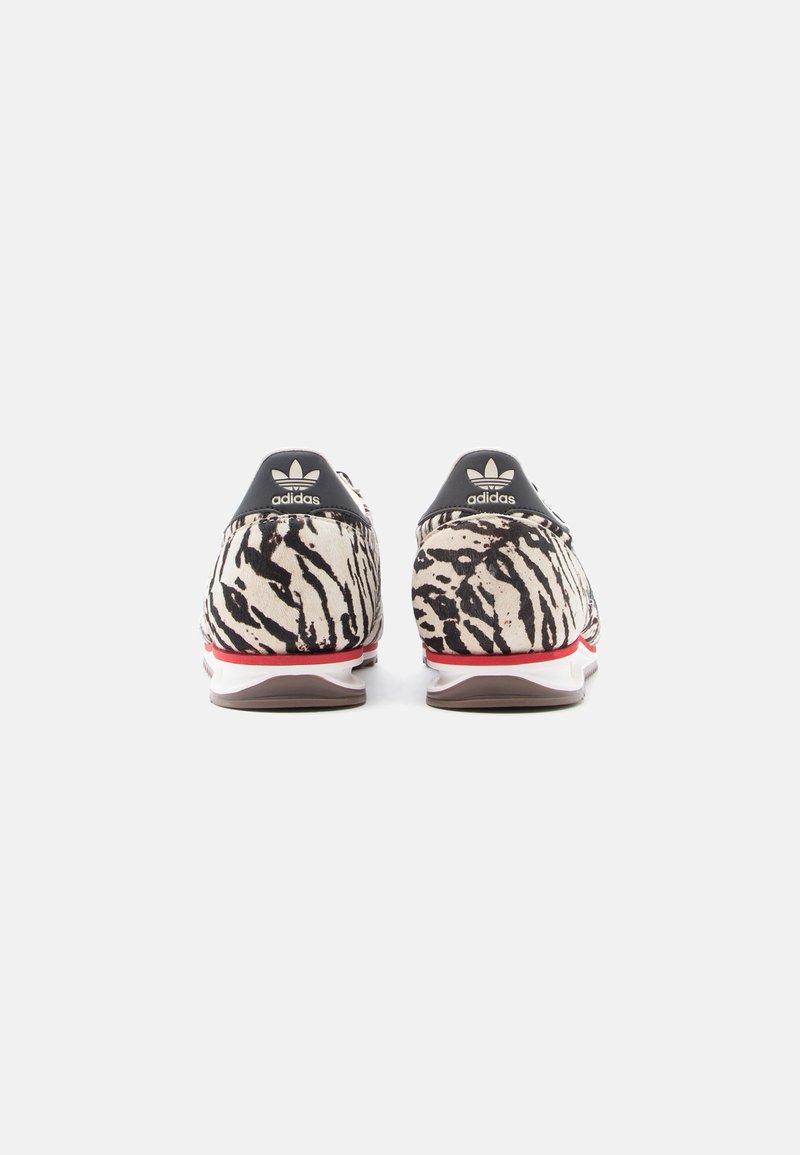 Adidas sneakers featuring a cream and black zebra print, with a red accent and black heel tab, made of textile material.