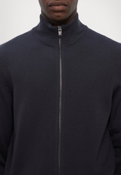 Dunkelblaues Zip-Up Sweatshirt mit strukturiertem Strick und hohem Kragen. Verfügt über einen Metallreißverschluss und dezente Details an den Schultern.
