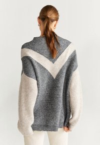 Pull en tricot gris et crème avec un motif de couleur en V, épaules tombantes et texture côtelée. Coupe décontractée avec des manches longues.