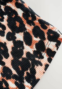 Tissu côtelé présentant un motif léopard noir et pêche. La texture est douce, avec des coutures visibles le long du bord.