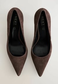 Mokkasin ruskeat sueded nilkkurit, joissa on sileä musta sisus ja matala leikkauksen design, joka luo elegantin siluetin.