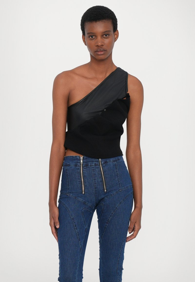 Schwarzes asymmetrisches Oberteil mit glatter Textur, kombiniert mit hoch taillierten blauen Jeans, die über doppelte Reißverschluss-Taschen und kantige Nähte verfügen.