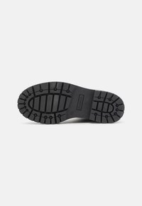 Semelle de botte en caoutchouc noir avec des crampons profonds, une forme arrondie et un motif texturé pour une meilleure adhérence. Marque distincte visible sur le côté.