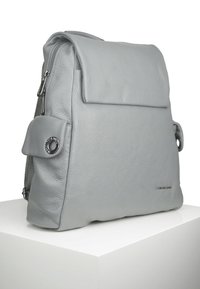Sac à dos en cuir gris avec une finition texturée, doté d'un rabat, d'un compartiment zippé et d'une poche latérale avec un accent circulaire.