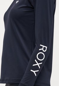 Jūrų laivyno ilgas rankovės marškinėliai, pagaminti iš lygaus audinio. Ranka dešinėje pusėje puikuojasi baltas "ROXY" tekstas, o ant krūtinės yra mažas logotipas.