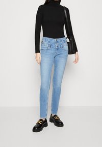 Jeans skinny azul claro con cierre de dos botones, cinco bolsillos y un sutil detalle de costura, combinados con un suéter de cuello alto negro y mocasines negros.