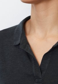 Dunkelgraues Polohemd mit weicher Textur, ausgestattet mit einem kleinen Kragen und einer kurzen Knopfleiste am Hals. Minimalistisches Design ohne Muster.