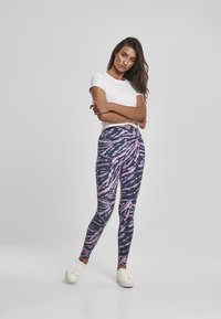 Leggings tamne tamnog osnovnog uzorka s ružičastim i plavim apstraktnim uzorkom. Izrađene od rastezljivog materijala, visokog struka, uparene s bijelim tenisicama.