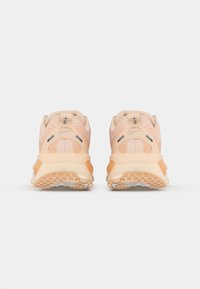 Baskets couleur pêche en matériaux synthétiques et en mesh, avec une semelle texturée, un col rembourré et des accents orange contrastants.