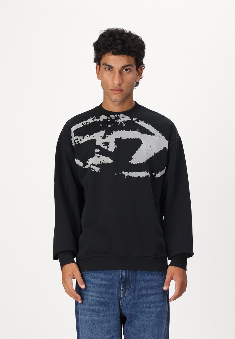 Sort sweatshirt lavet af blødt stof med et stort gråt abstrakt mønster på fronten, ribbet krave, manchetter og kant. Parret med blå jeans.