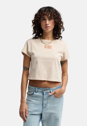 Beige cropped t-shirt van katoen met korte mouwen, voorzien van een oranje grafische print en gedragen met lichtblauwe spijkerbroek.