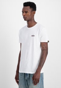 Hvid bomulds T-shirt med rund hals, korte ærmer og et lille sort og rødt grafisk motiv på brystet; har en logoed ærmekant.