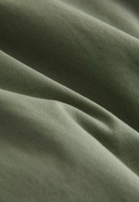 Gros plan sur un tissu vert olive plié montrant une texture lisse et des détails de couture fins.