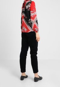 Blusa a fiori rossa e nera con maniche lunghe, abbinata a pantaloni in corduroy neri e scarpe basse nere, vista da dietro.